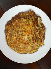 Omelet with carrot and onion on white plate, top view