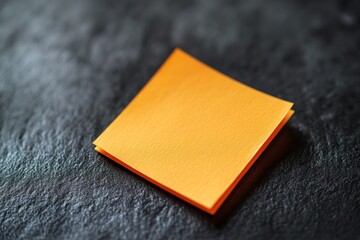 Simple stack of bright orange sticky notes on a dark textured surface creates a striking visual contrast for office organization