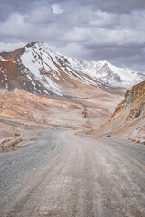 Dusty high-mountain road of Pamir Highway and Ak-Baital Pass, panoramic landscape in rocky mountains with snow in Tien Shan Mountains in Tajikistan