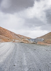 Dusty high-mountain road of Pamir Highway and Ak-Baital Pass, panoramic landscape in rocky mountains with snow in Tien Shan Mountains in Tajikistan