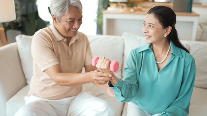 Obraz premium Happy elderly couple exercising together with dumbbells at home, focusing on muscle strength, joint health, and physical wellness for improved mobility and healthy aging. Retirement concept. Myrmidon.