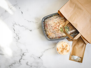 Noodles with vegetables in a container and dessert on the table.