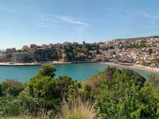Naklejka premium A picturesque coastal town with turquoise waters, lush green vegetation and white buildings under a clear blue sky.