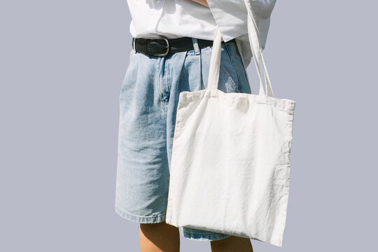 Woman hand holding eco bag. Female hold white canvas textille mesh zero waste shopper isolated on light grey minimal wall background.. Blank mock up tote bag, place for text design logo.