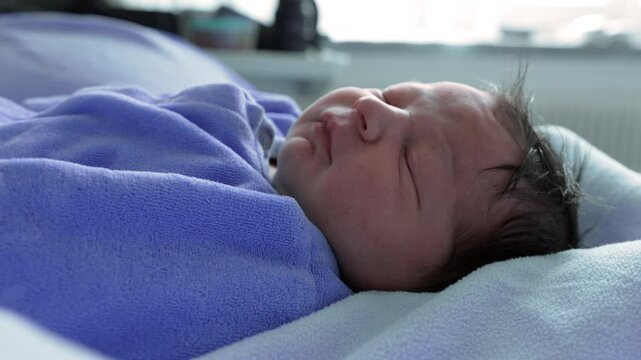 Newborn baby sleeping soundly in a hospital bassinet, swaddled in a blue blanket, capturing the delicate and peaceful early moments of life, emphasizing innocence and serenity