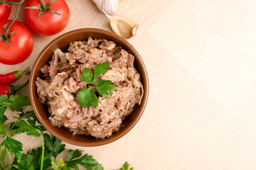 Canned meat in bowl, parsley, tomatoes and garlic on wooden table, top view. Space for text