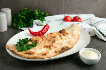 Delicious calzone served with sauce on grey table