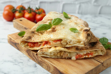 Halves of tasty calzone with meat, cheese, basil and tomato on white marble table, closeup