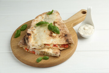 Halves of tasty calzone with meat, cheese, tomato, basil and sauce on white wooden table, closeup