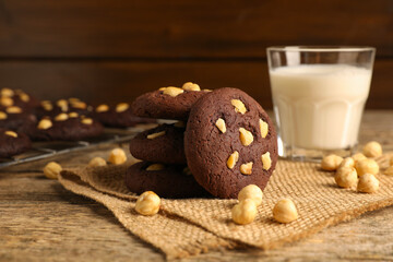 Tasty chocolate cookies with hazelnuts and milk on wooden table, closeup