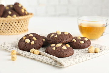Tasty chocolate cookies with hazelnuts and tea on white table, closeup