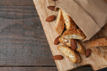 Paper bag with tasty almond biscuits (Cantuccini) and nuts on wooden table, top view. Space for text