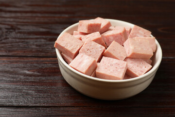 Pieces of canned meat in bowl on wooden table, closeup