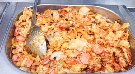 Cabbage stir-fry with sausages displayed in a food serving tray at a community event
