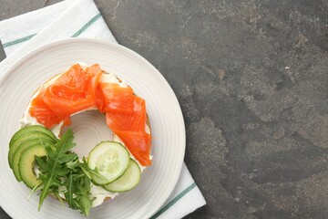 Delicious bagel with salmon, cream cheese, cucumber and avocado on grey table, top view. Space for text
