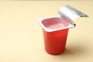 Delicious yogurt in plastic cup on beige background, closeup. Space for text