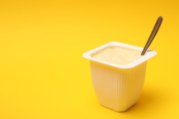 Delicious yogurt in plastic cup on yellow background, closeup. Space for text