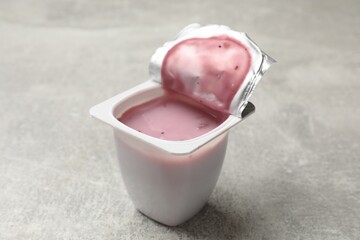 Delicious yogurt in plastic cup on gray textured table, closeup
