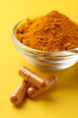Turmeric powder in bowl and capsules on yellow background, closeup