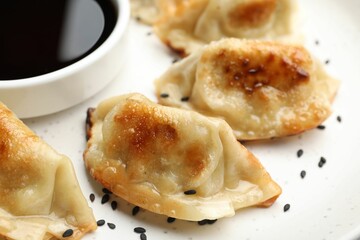 Fried gyoza dumplings with sesame seeds and soy sauce on table, closeup