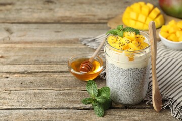 Delicious chia pudding with mango in glass, mint and honey on wooden table, closeup. Space for text