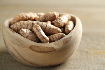 Raw turmeric roots in bowl on wooden table, closeup