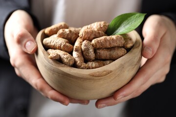 Woman holding bowl with raw turmeric roots, closeup