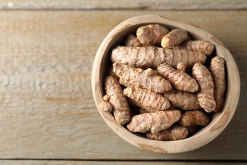 Raw turmeric roots in bowl on wooden table, top view. Space for text