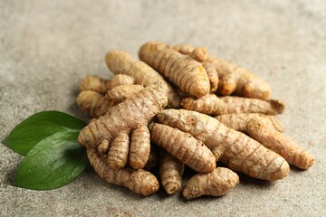 Pile of tumeric rhizomes with leaves on grey table, closeup