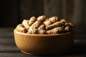 Tumeric rhizomes in bowl on wooden table, closeup