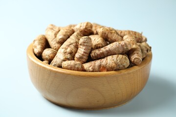 Tumeric rhizomes in bowl on light blue background, closeup