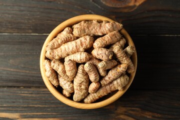 Tumeric rhizomes in bowl on wooden table, top view