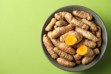 Tumeric rhizomes in bowl on green background, top view. Space for text