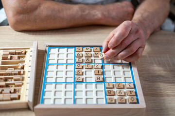 closeup hands carefully placing number into Sudoku puzzle, senior man focused on solving puzzle on...