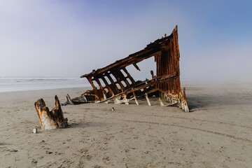 Rusty shipwreck on a foggy beach. Ocean waves crash nearby. Nature's reclamation. Wreck Of The...