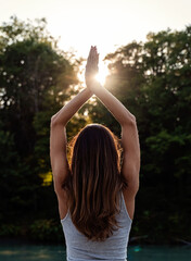 Back rear view of happy young woman standing at nature with hands up meeting the sun doing yoga. Harmony and connection with nature, meditation