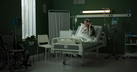 Young woman in a hospital bed relaxes with headphones on.