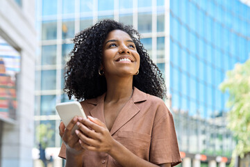 Happy professional African American business woman holding smartphone looking away with cellphone...