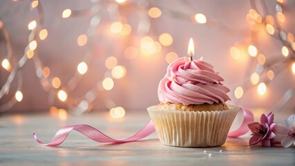 A delicate pink cupcake with a sparkling candle on top, surrounded by candles and ribbons