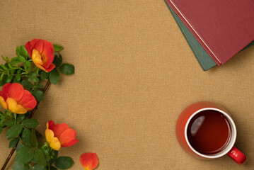 Rosehip flowers, books, cup of tea on fabric background. Flat lay, top view.