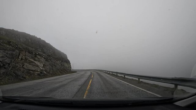 Driving through the tundra in northern Norway on E69 road. Surrounded by misty hills and rocky cliffs, creating a dramatic and serene landscape.