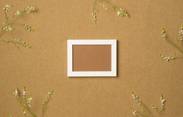 Empty photo frame with frame of flowers on fabric background. Flat lay, top view.