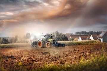 bauer auf traktor erntet den boden bei schönen himmel und wohnungen im hintergrund © thebigticket20