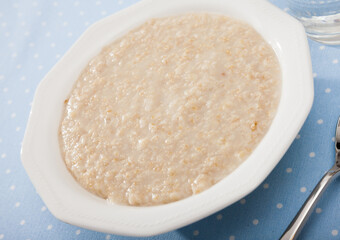Boiled oatmeal porridge served in white plate. Concept of diet food..