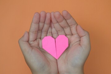 Fototapeta premium Woman's hand holding pink love shape origami paper