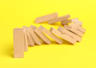 Domino effect. Wooden blocks falling on yellow background, closeup