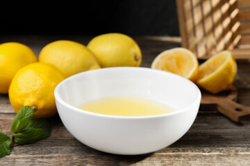 Fresh lemon juice in bowl and fruits on wooden table, closeup