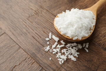 Spoon with white soy wax flakes on wooden table, closeup. Space for text