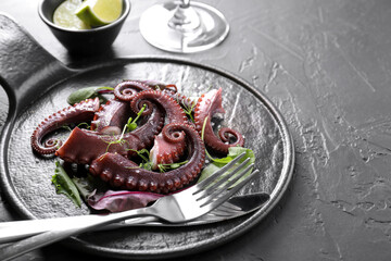Tasty boiled octopus tentacles, microgreens and cutlery on grey textured table, closeup
