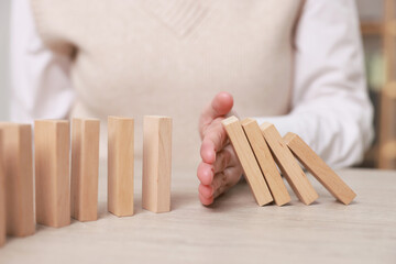 Woman stopping wooden blocks from falling at table, closeup. Domino effect